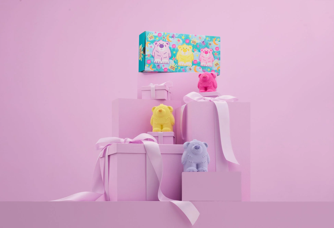 リボンがかかったギフトボックスが階段状に積まれ、その上にカラフルなクマの形をした商品