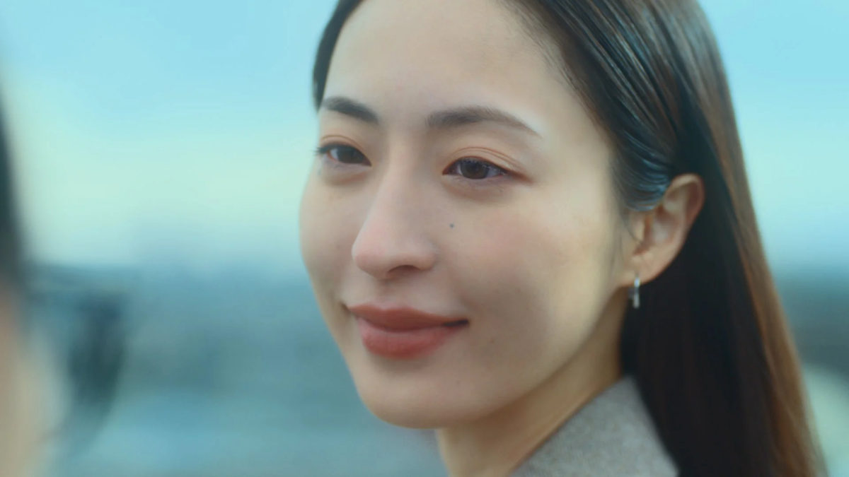 明るい屋外で、少し横を向いて優しく微笑む女性の顔のクローズアップ