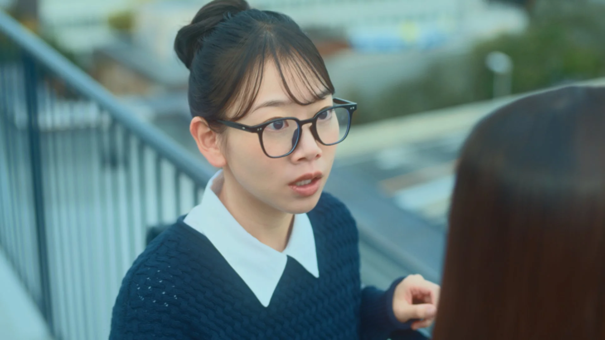 眼鏡をかけた若い女性が屋外で誰かと会話している様子