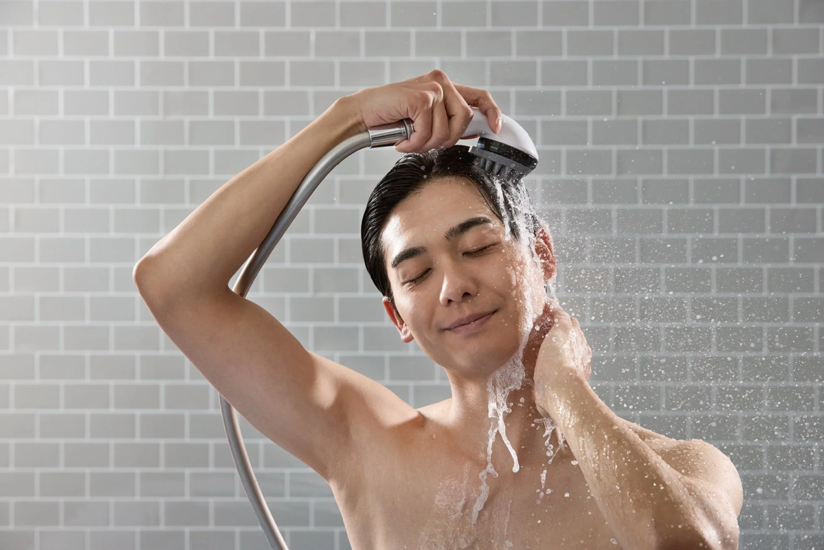シャワーを浴びて髪と顔を洗う男性