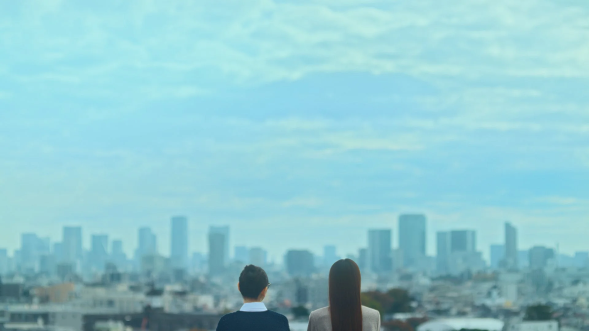 二人の人物が都会のビル群が広がる景色を背にして見つめている様子