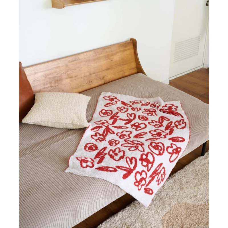 ベージュのリブ編みクッションが敷かれた木製ベンチに、赤色の抽象的な花柄が描かれた白いブランケット