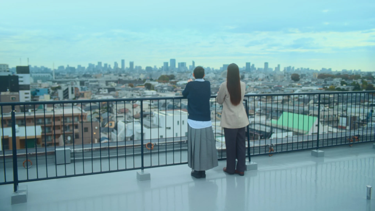 屋上から都市の街並みを眺める二人の人物の後ろ姿