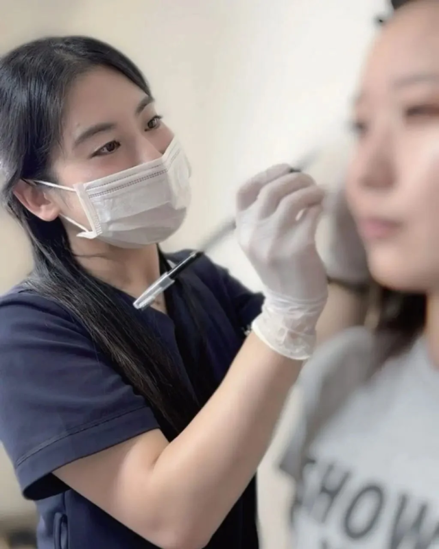 マスクとグローブを着用した施術者が女性の顔に美容施術を行っている様子