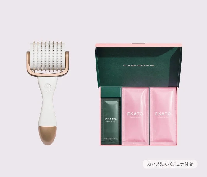画像には、白いハンドルとゴールドのヘッドを持つローラーと、ピンクと深緑色の箱に入った美容製品セットが写っています。箱の中には「EKATO.」ブランドの炭酸ジェルパックが複数個と、緑色の容器が入っており、箱の蓋には「TO THE NEXT SKIN OF MY LIFE」と書かれています。