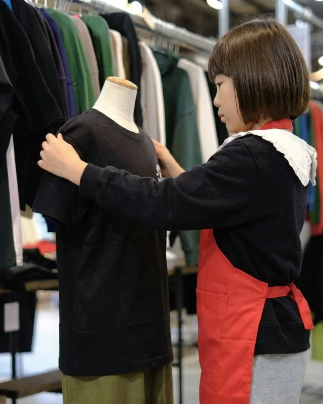 赤いエプロンをつけた子供がマネキンのTシャツを整えている様子
