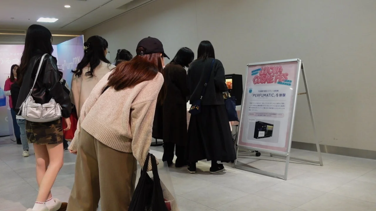 ルクアコスメフェスの会場で、複数の女性が「PERFUMATIC」という香りディスプレー自動機の体験ブースを見ている様子。イベントの賑わいが感じられます。