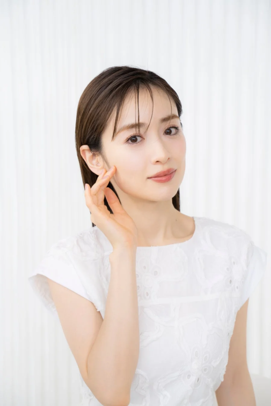 白いトップスを着た女性が、右頬に手を当てて優しく微笑んでいるポートレート写真