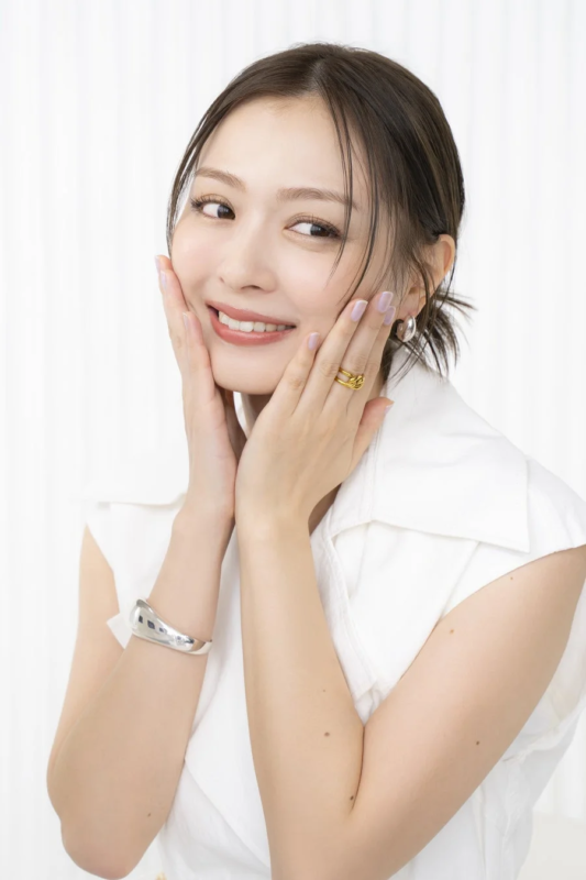 白いノースリーブのトップスを着た日本人女性が、両手を頬に当てて優しく微笑んでいます