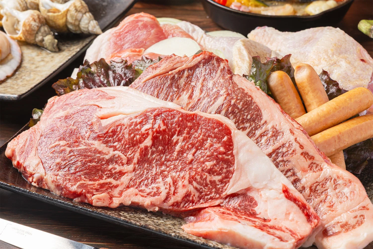 霜降りの牛肉ステーキ、鶏肉、豚肉、ソーセージ、サザエ、ホタテなどが豪華に盛り合わせられた、焼肉やBBQにぴったりの新鮮な食材の画像です。
