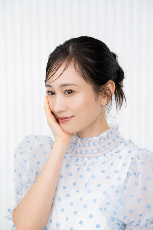 白い水玉模様のブラウスを着た日本人女性が、頬に手を当てて優しく微笑むポートレート