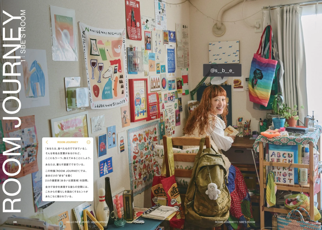 「ROOM JOURNEY」特集に登場する、個性と「好き」が詰まった部屋で笑顔を見せる女性。壁にはポスターやアートが所狭しと飾られ、カラフルな雑貨が溢れる、彼女らしいライフスタイルが垣間見える空間。