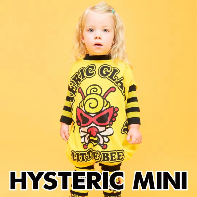 金髪の幼児が、黄色い蜂のキャラクターと「LITTLE BEE」の文字がプリントされた黄色い服を着て立っています。背景も黄色で、「HYSTERIC MINI」のロゴも見えます。