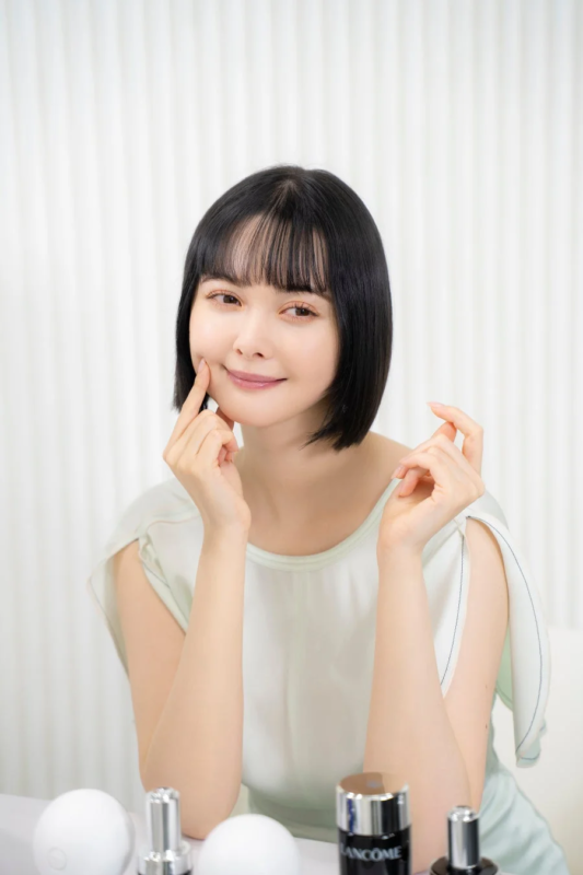 短い黒髪の女性が笑顔で頬に指を当てています