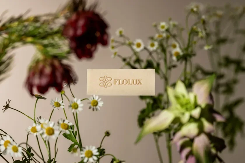 FLOLUXと書かれたベージュのバーが、様々な花々に囲まれて配置されている製品写真