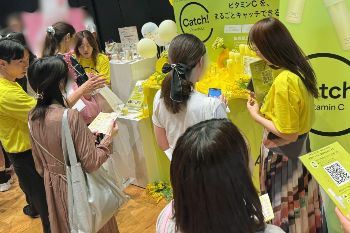 黄色の装飾が施されたイベントブースで、複数の人々が製品を見ている様子