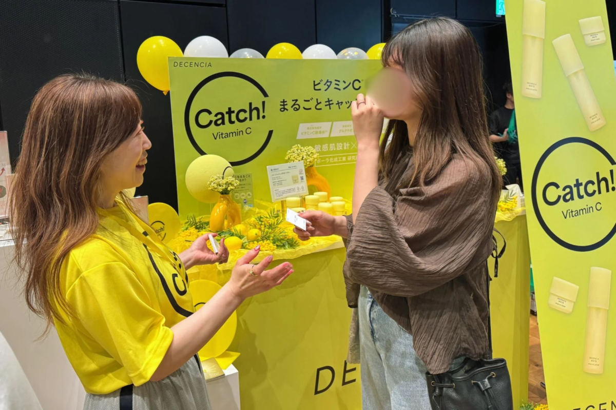 DECENCIAのビタミンC配合スキンケア製品のプロモーションイベントで、女性スタッフが来場者に説明している様子