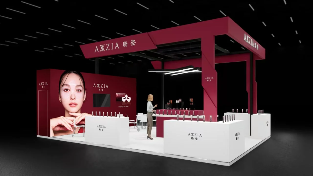 AXZIAのブランドブースで、赤と白を基調としたモダンなデザインが特徴です。女性モデルの大型写真や化粧品が多数展示されており、美容イベントの様子を伝えています。
