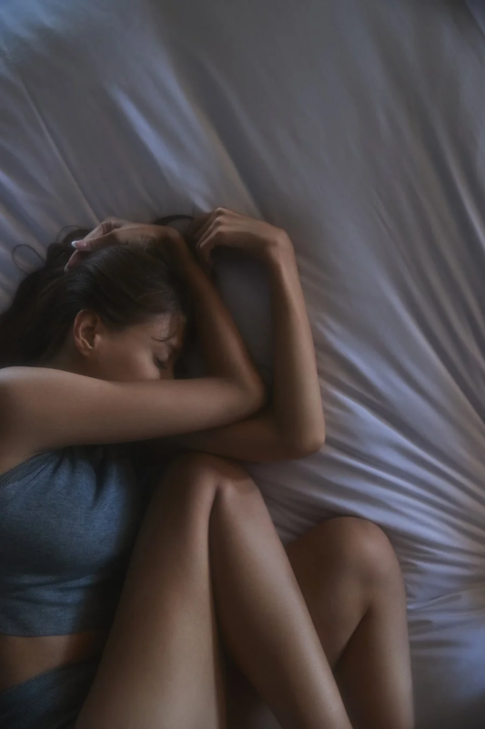 ベッドで横たわる女性が、腕を抱え込み、安らかに眠っている様子を捉えた画像です。