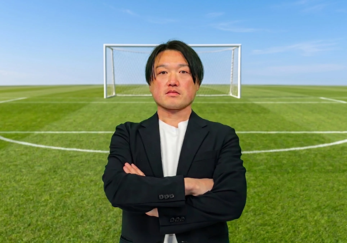 サッカー場を背景に腕組みする男性