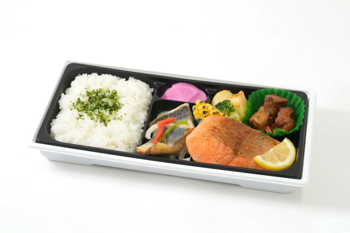 白飯、鮭の切り身、魚のフライ、鶏肉の煮物、ブロッコリー、ポテト、コーン、漬物などが入ったバランスの良い和風弁当です。テイクアウトやランチに最適です。