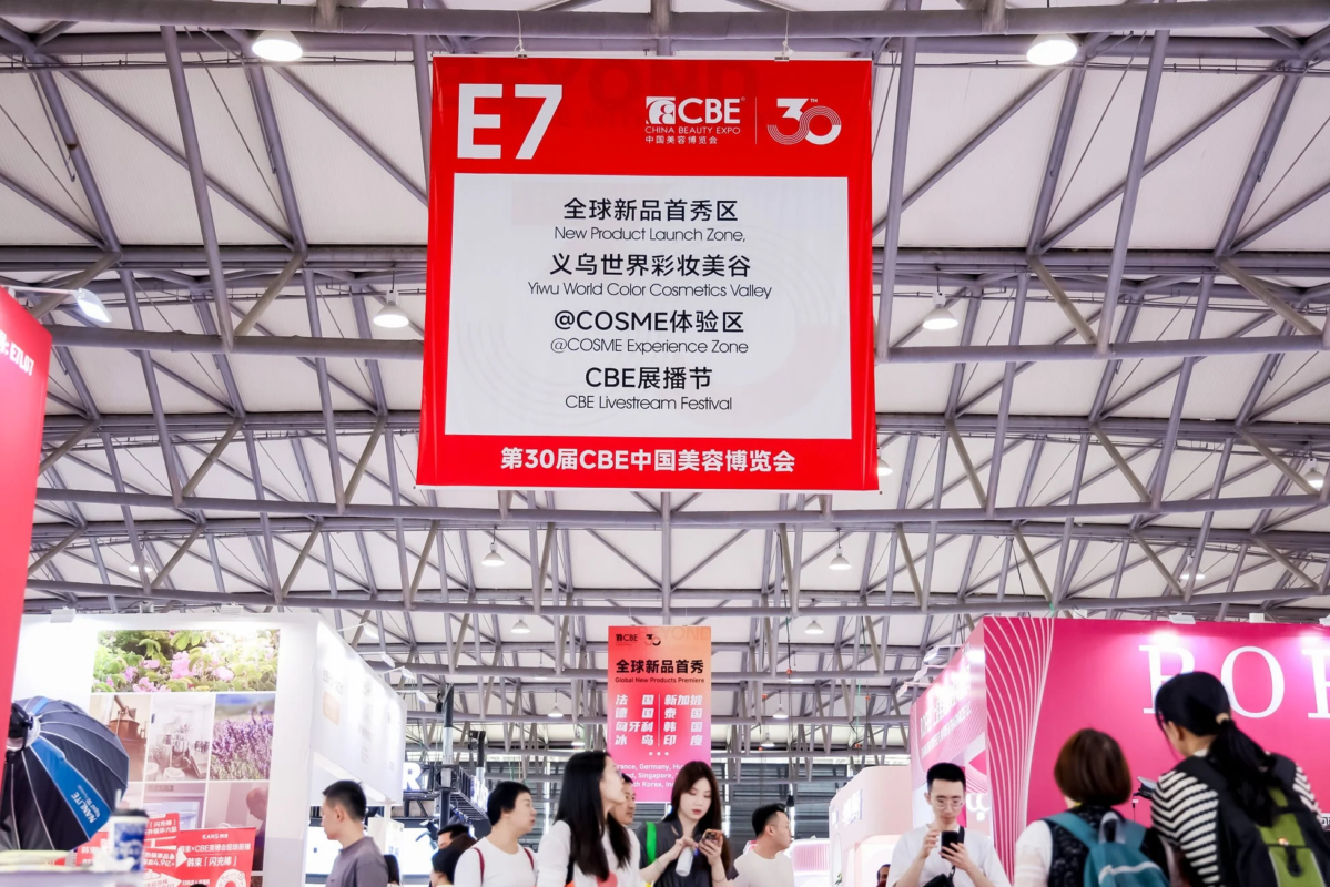 第30回CBE中国美容博覧会の賑やかな会場風景。新製品発表ゾーンや@COSME体験ゾーンなどの情報が記載された赤い大型バナーが目立ち、多くの来場者が行き交っている。