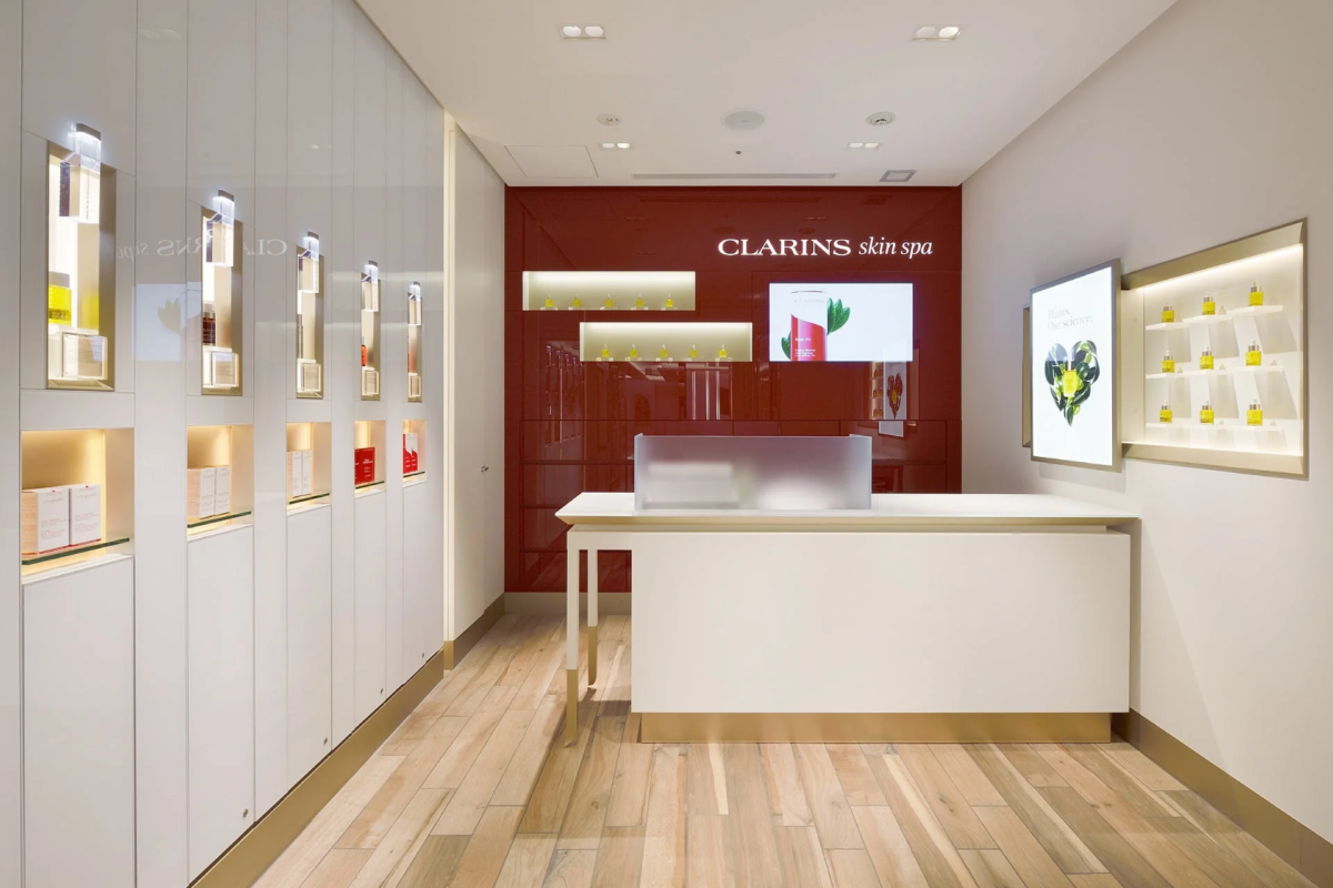 CLARINS skin spaのモダンで洗練された店舗内観。赤と白を基調とした空間に、スキンケア製品が美しくディスプレイされ、中央には受付カウンターが配置されています。
