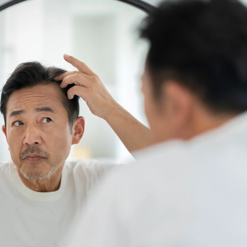 鏡を見ながら自分の髪を気にしているアジア人男性