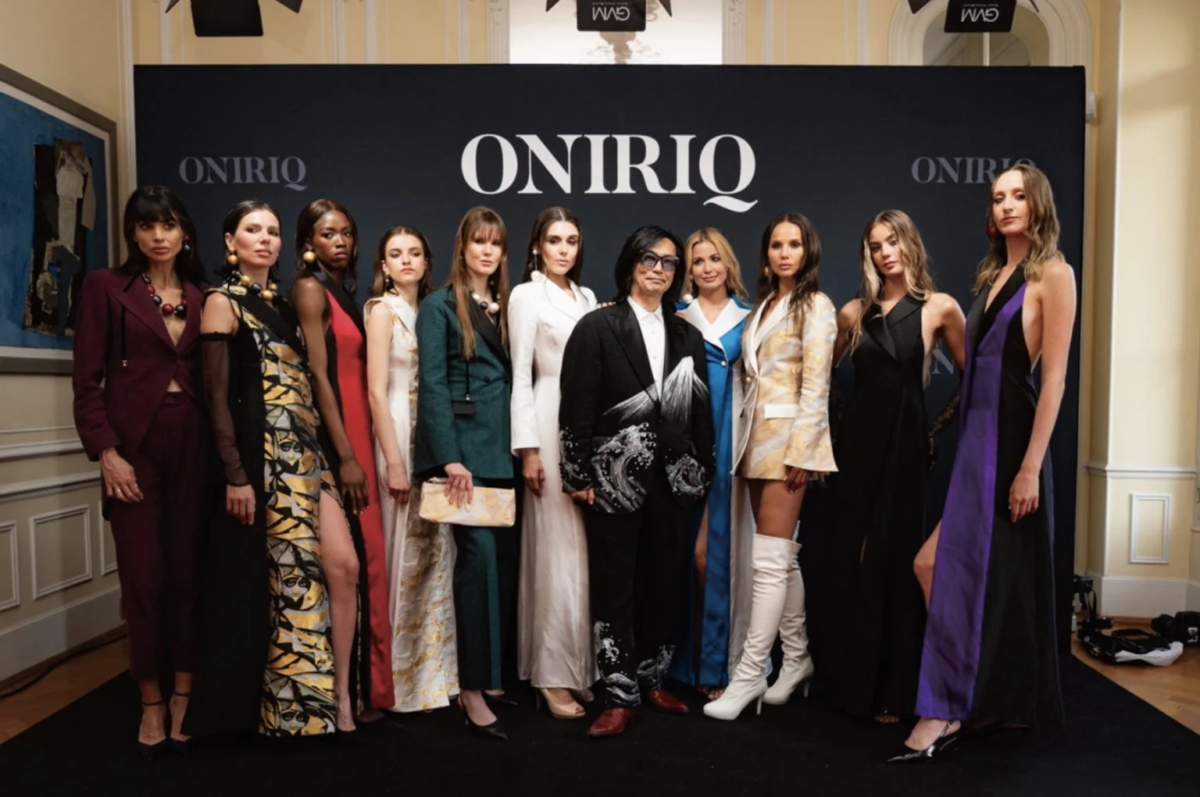 「ONIRIQ」のロゴを背景に、デザイナーと様々なデザインの華やかな衣装をまとったモデルたちが並んでポーズをとっています