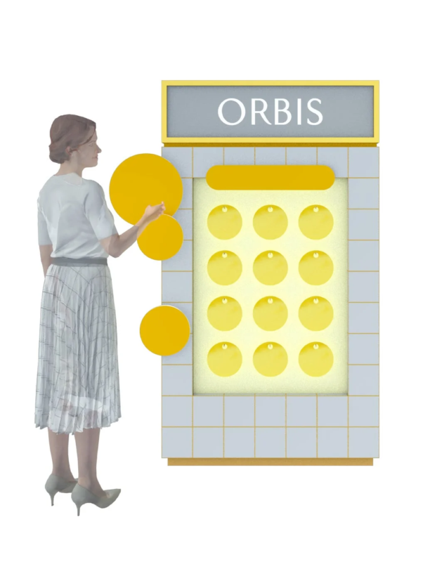 女性が「ORBIS」と書かれたディスプレイの横に立ち、黄色い丸い商品を指差しています