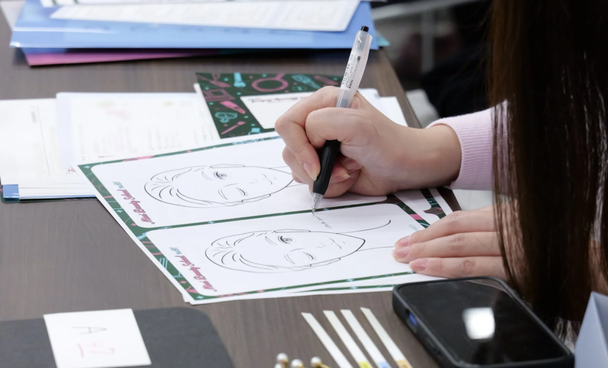 美容学校のような場所で、女性が顔のイラストが描かれたシートにペンで書き込んでいる様子