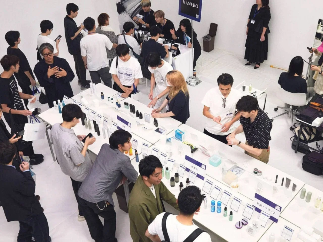 カネボウのスキンケア製品が展示されたイベント会場で、多くの参加者が集まり、商品の説明を聞いたり試したりしています。スタッフがデモンストレーションを行う様子も見られ、活気のある美容イベントの様子が上から捉えられています。
