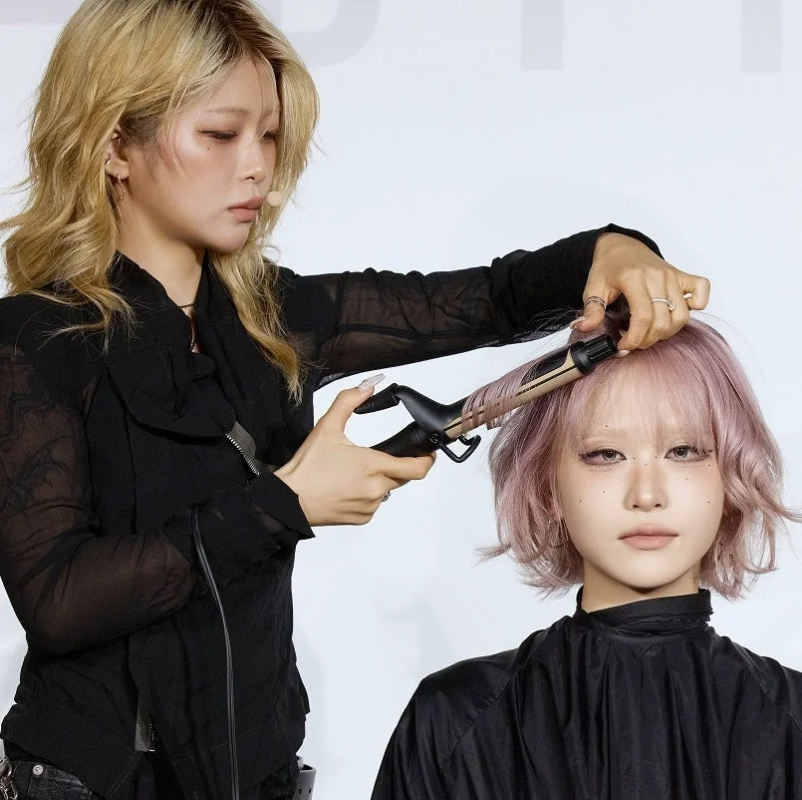 美容師がピンク色のショートヘアのモデルの髪をカールアイロンでスタイリングしている様子