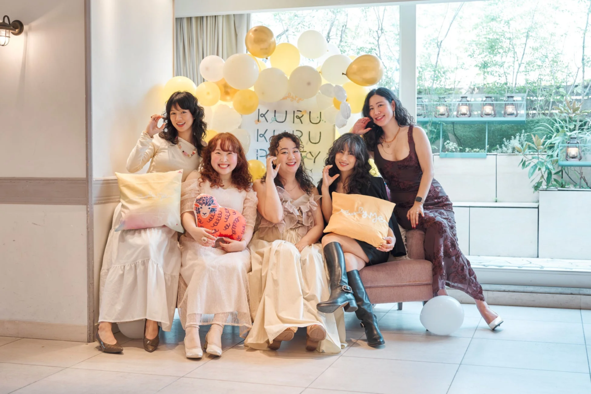 5人の女性が笑顔でポーズをとっており、背景には「KURU KURU PARTY」と書かれたバナーとたくさんの風船が飾られています