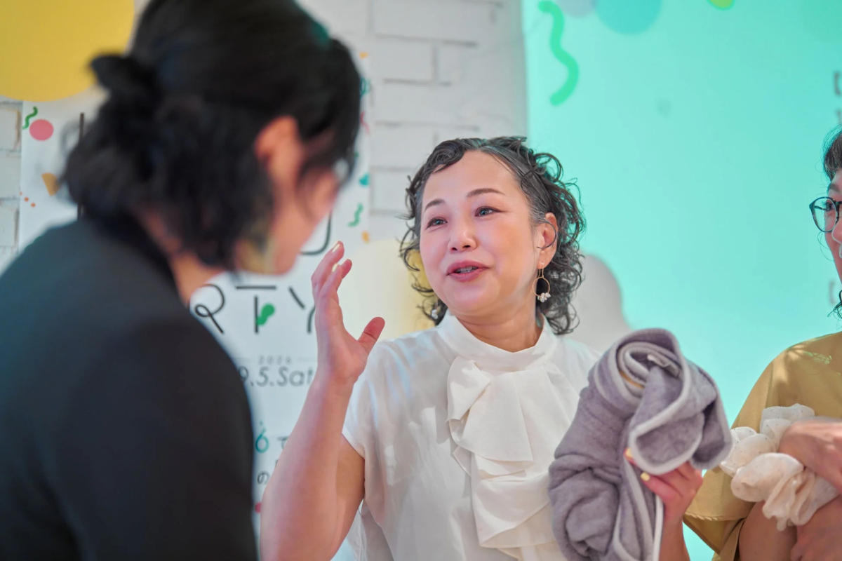 室内イベントで、一人の女性がもう一人の女性に向かって、手振り身振りを交えながら楽しそうに話しています