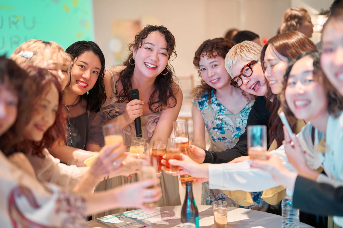多くの女性たちが集まり、笑顔でグラスを掲げて乾杯している賑やかな交流会の様子
