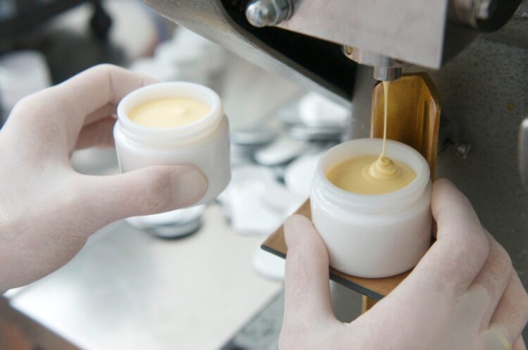 Hands filling cream into a white container