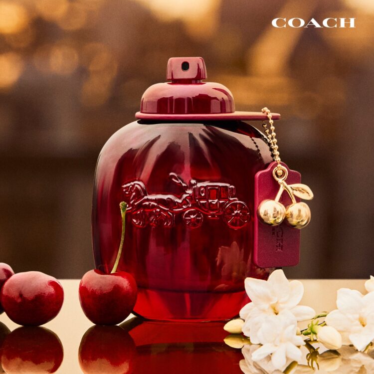 放在白花和樱桃旁的红色Coach Cherry Parfum瓶身