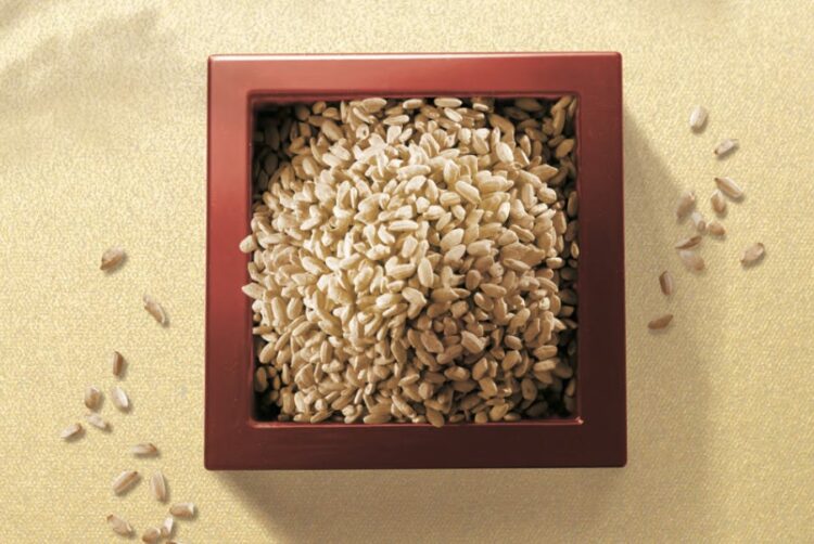 Brown rice in a wooden box, with grains scattered around it