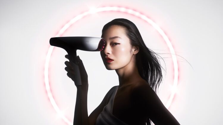 ヘアドライヤーを手にしたモデルと、背景に広がるピンクの光の輪