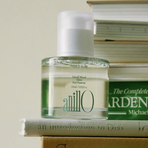 A bottle of Neroli Wood Glow Hair Essence placed on a book