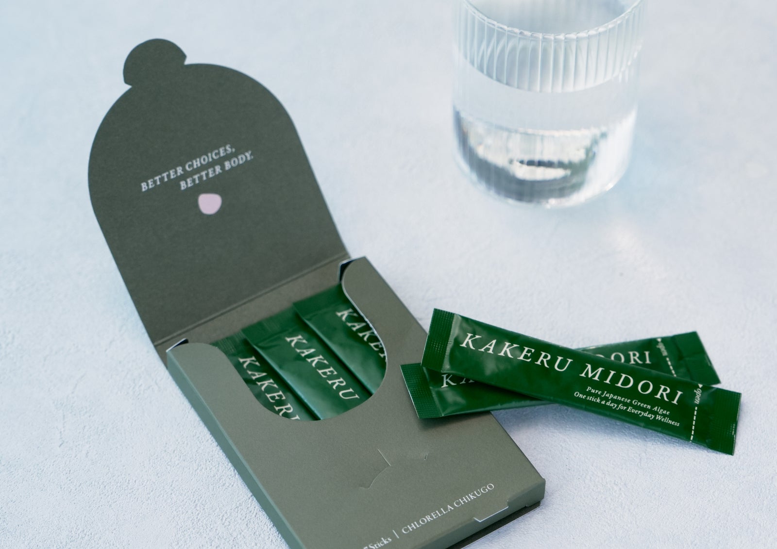 個包装のクロレラパウダー『KAKERU MIDORI』と、水の入ったグラス