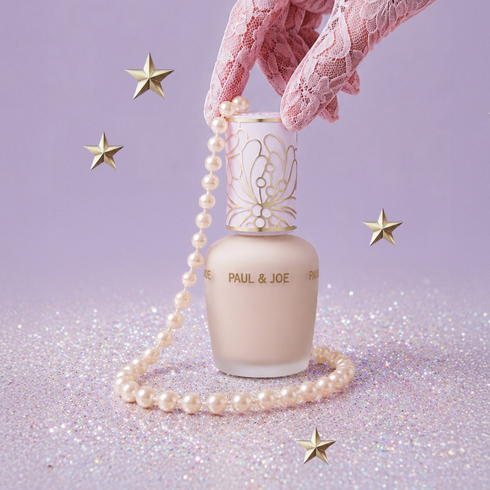 パールのネックレスと星に囲まれた、淡いピンクベージュのPAUL & JOE BEAUTE ラトゥー エクラ プライマーのボトル