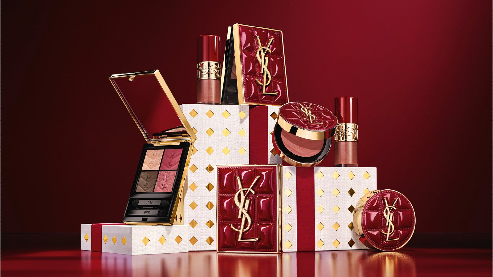 深紅の背景に、クチュール ミニ クラッチ、グロス、チークなどYSL BEAUTYのホリデー限定アイテムを並べたビジュアル