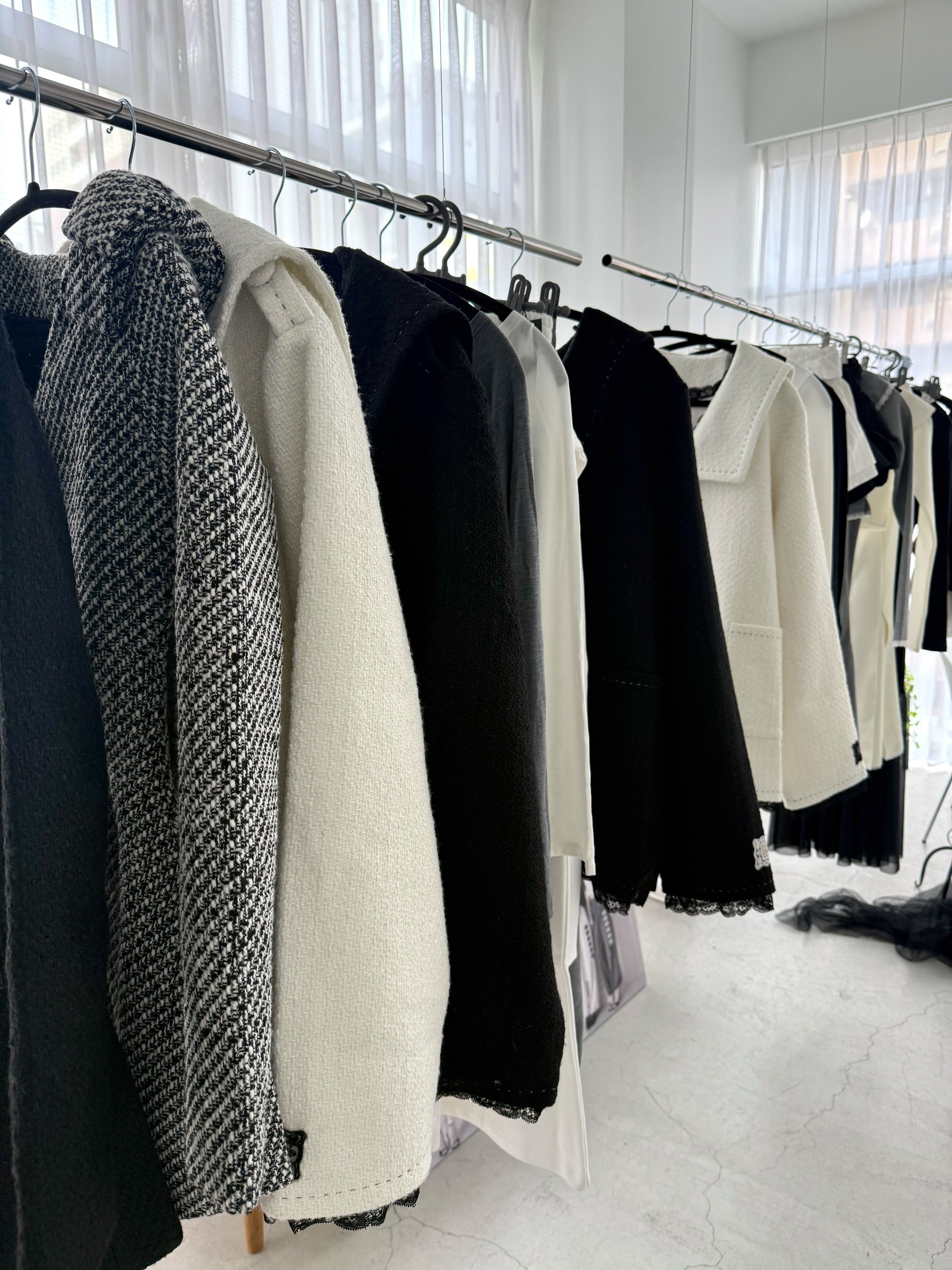 白や黒を中心とした衣服が並ぶ展示会のラック