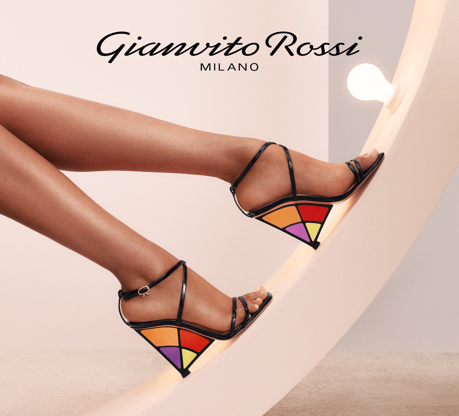ステンドグラス風の配色のヒールを持つサンダルを履いた脚。Gianvito Rossiのロゴ入りビジュアル
